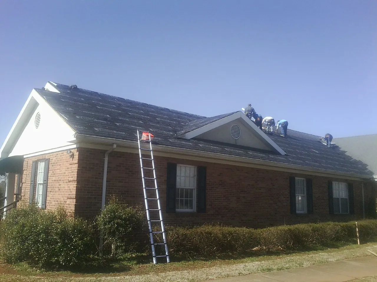 Crew tearing shingles off a brick ranch roof with a ladder set — Metal Roof Repair work by our crew in New Berlinville