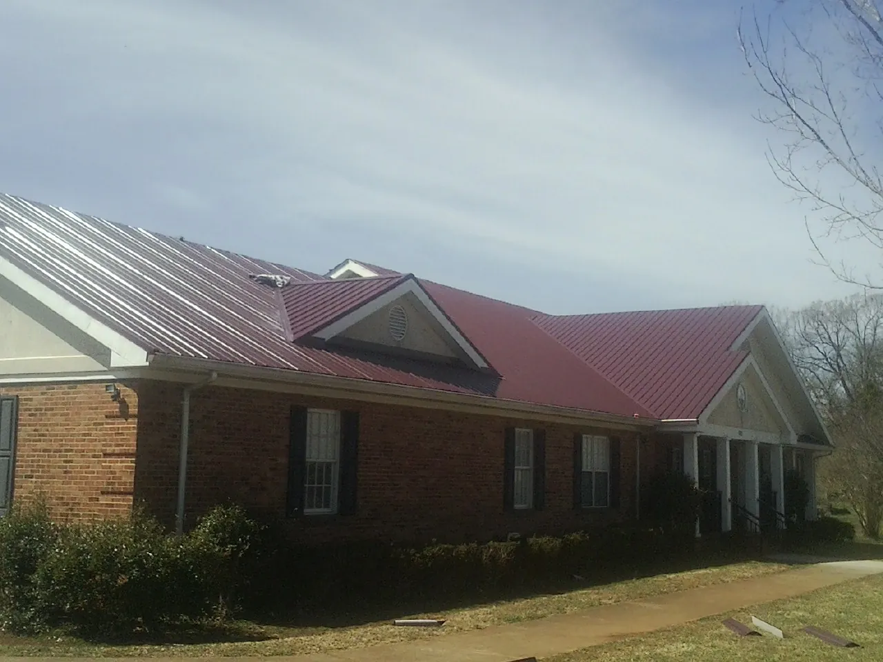 Red metal roof with gabled entries on a long brick building, from a Hail Damage Roof Repair job in New Berlinville