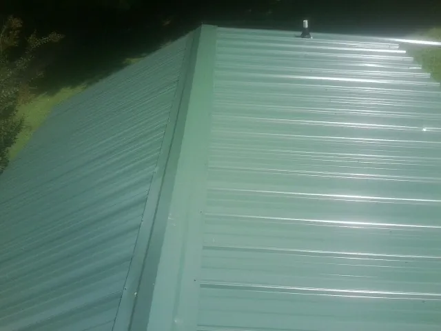 New green metal panels meeting at the ridge of a roof — Flat Roof Repair work by our crew in New Berlinville