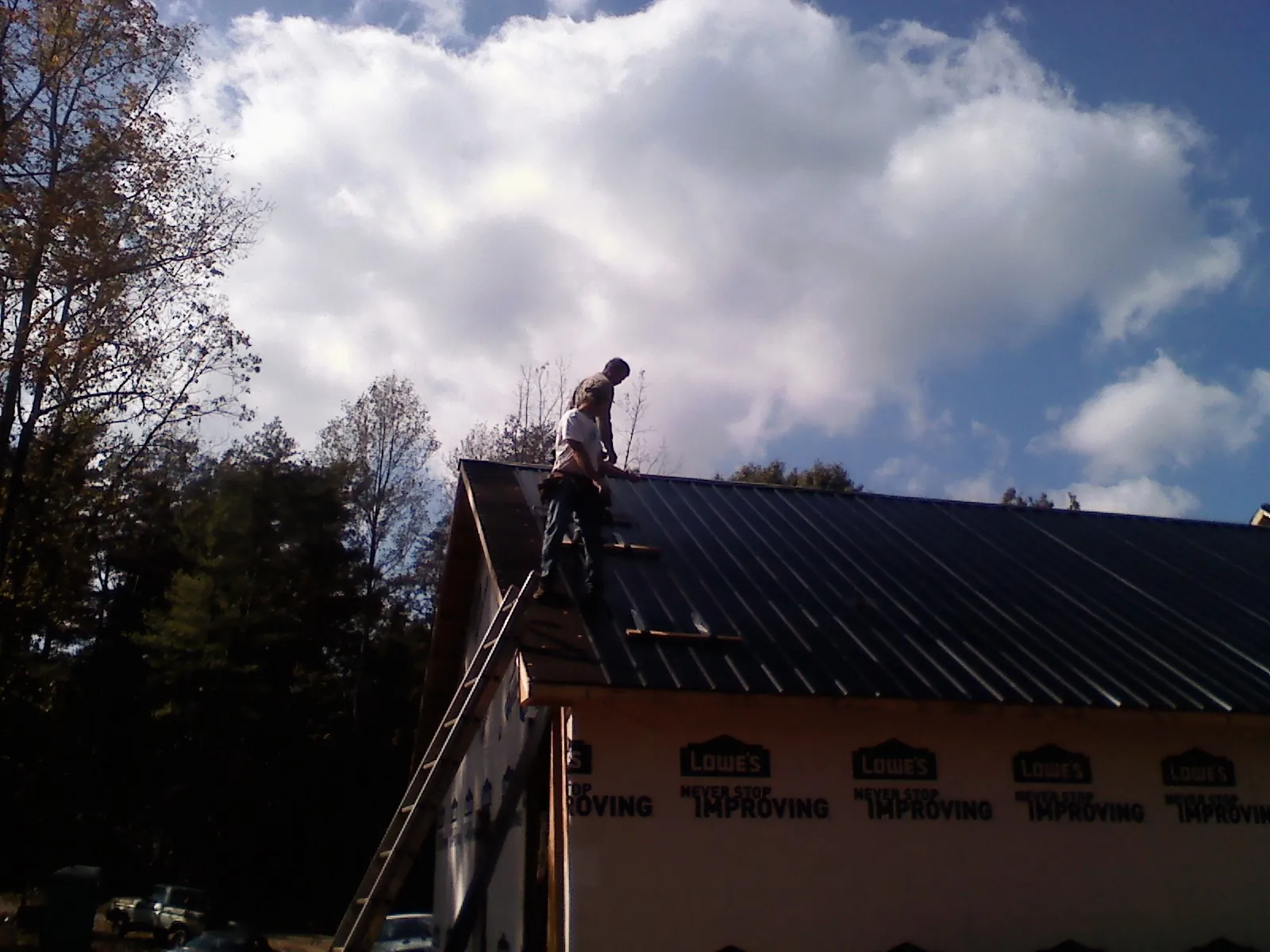 Roofer fastening dark metal panels high against a cloudy sky, from a Roof Inspection job in New Berlinville