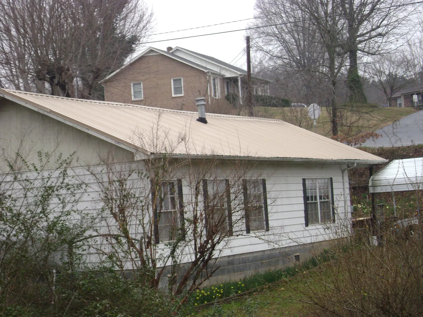Tan metal roof on a white sided house set into a hillside — Commercial Roofing by Roofing Brothers in New Berlinville